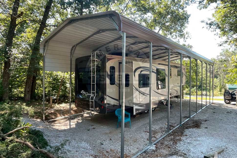 An RV parked under a metal roof in a wooded area, ready for summer travel preparations.