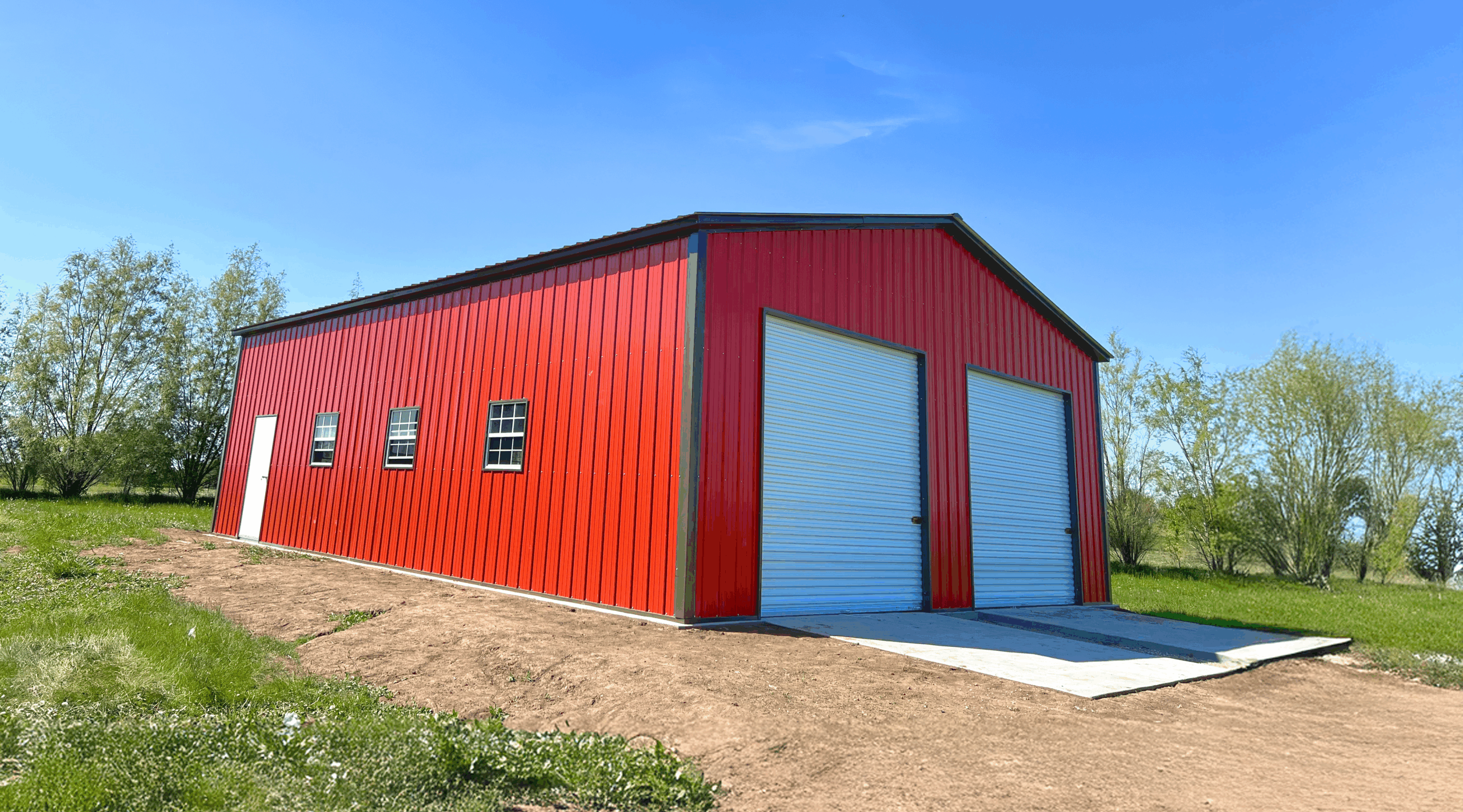 A red two-car metal garage in Abilene, Texas, side profile featuring white roll-up doors, three windows, a walk-in door, and a durable steel structure built by American Steel Carports, Inc.