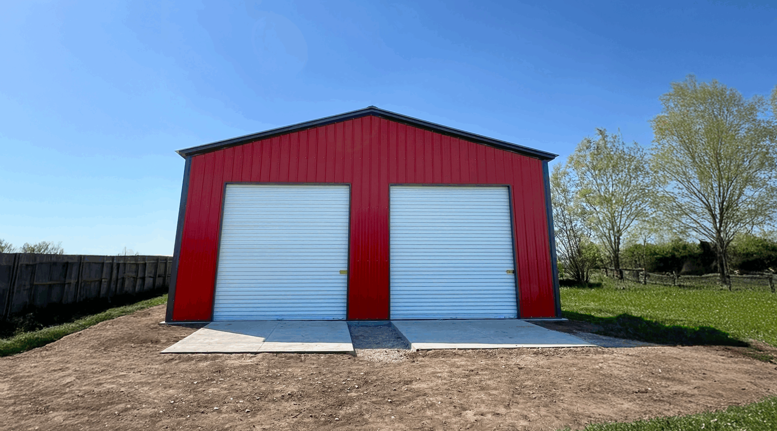 A red two-car metal garage in Abilene, Texas, featuring white roll-up doors and a durable steel structure built by American Steel Carports, Inc.