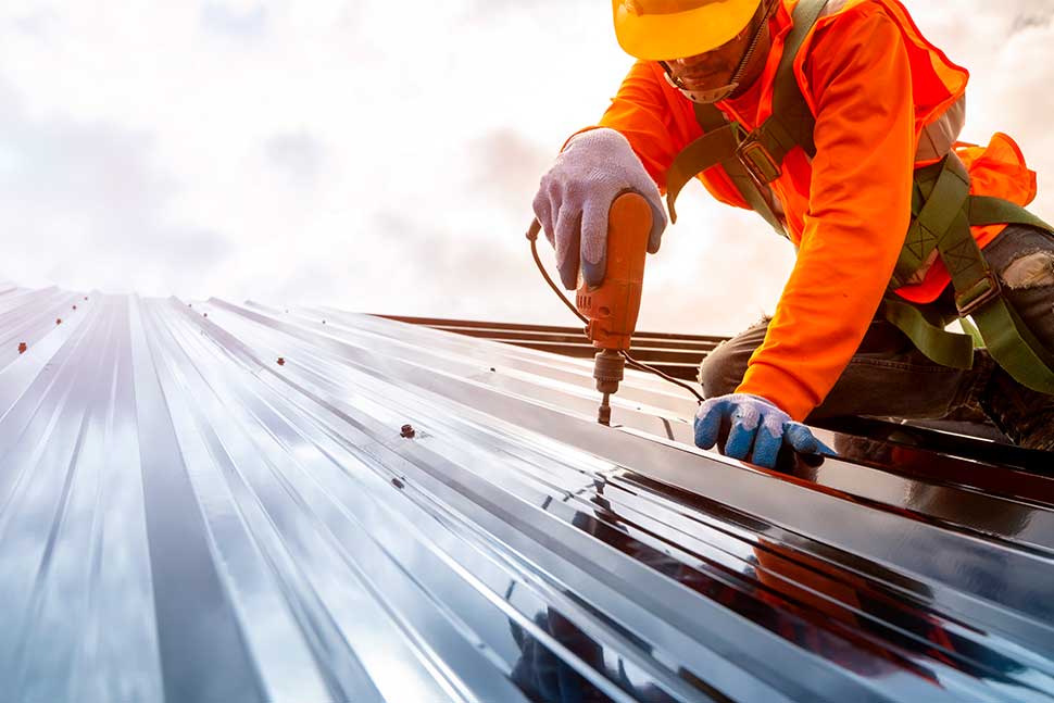 A man in orange safety gear works on a metal roof, highlighting safety practices for Texas summer roofing projects.
