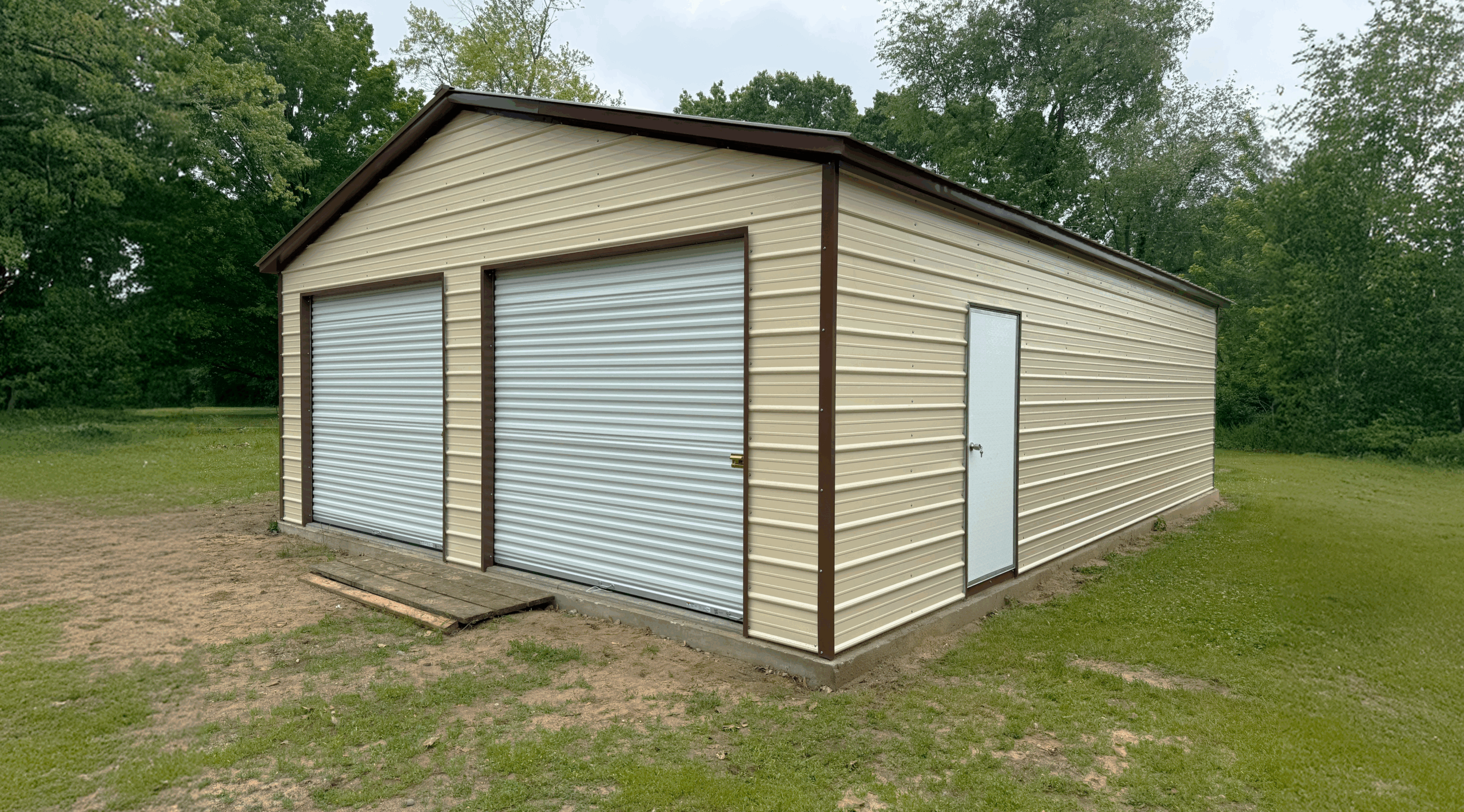 Pebble beige two-car metal garage with earth brown trim, white roll-up doors, and a side walk-in door, installed in Albany, KY by American Steel Carports, Inc.