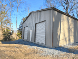Clay clear span metal garage with two white roll-up doors and a side walk-in door, built in Addison, TX by American Steel Carports, Inc.