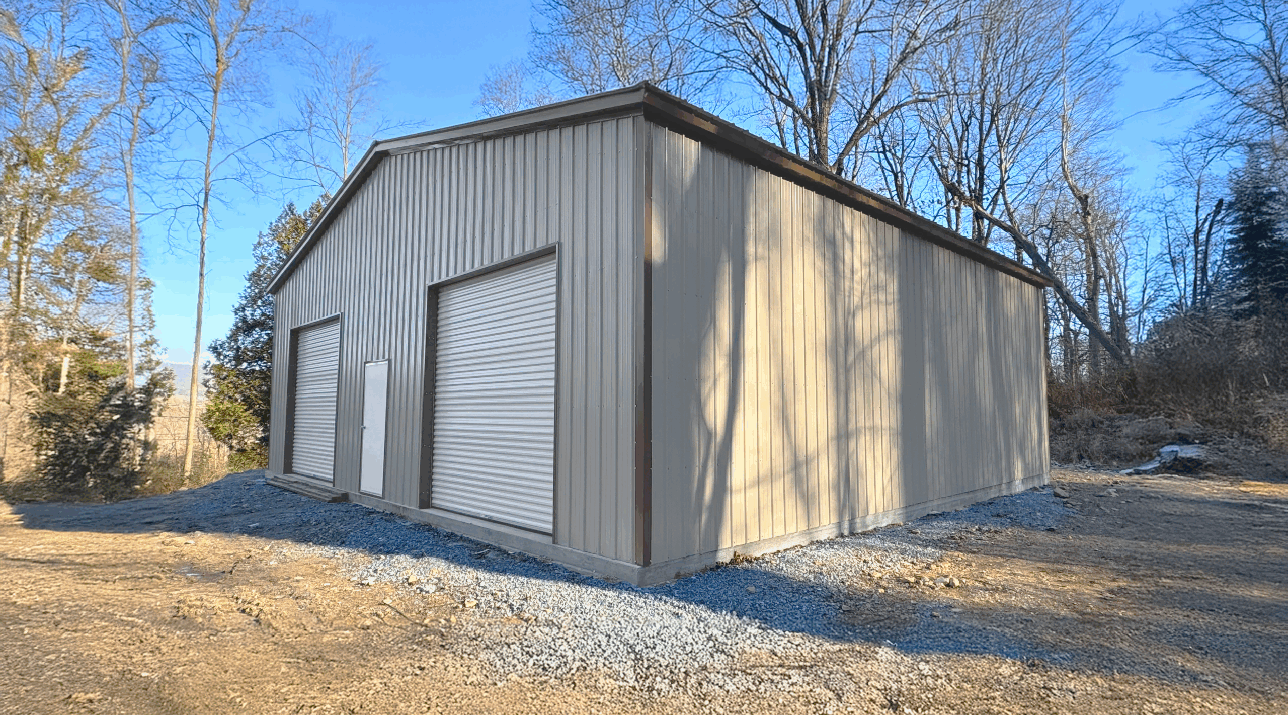 Clay clear span metal garage with two white roll-up doors and a side walk-in door, built in Addison, TX by American Steel Carports, Inc.