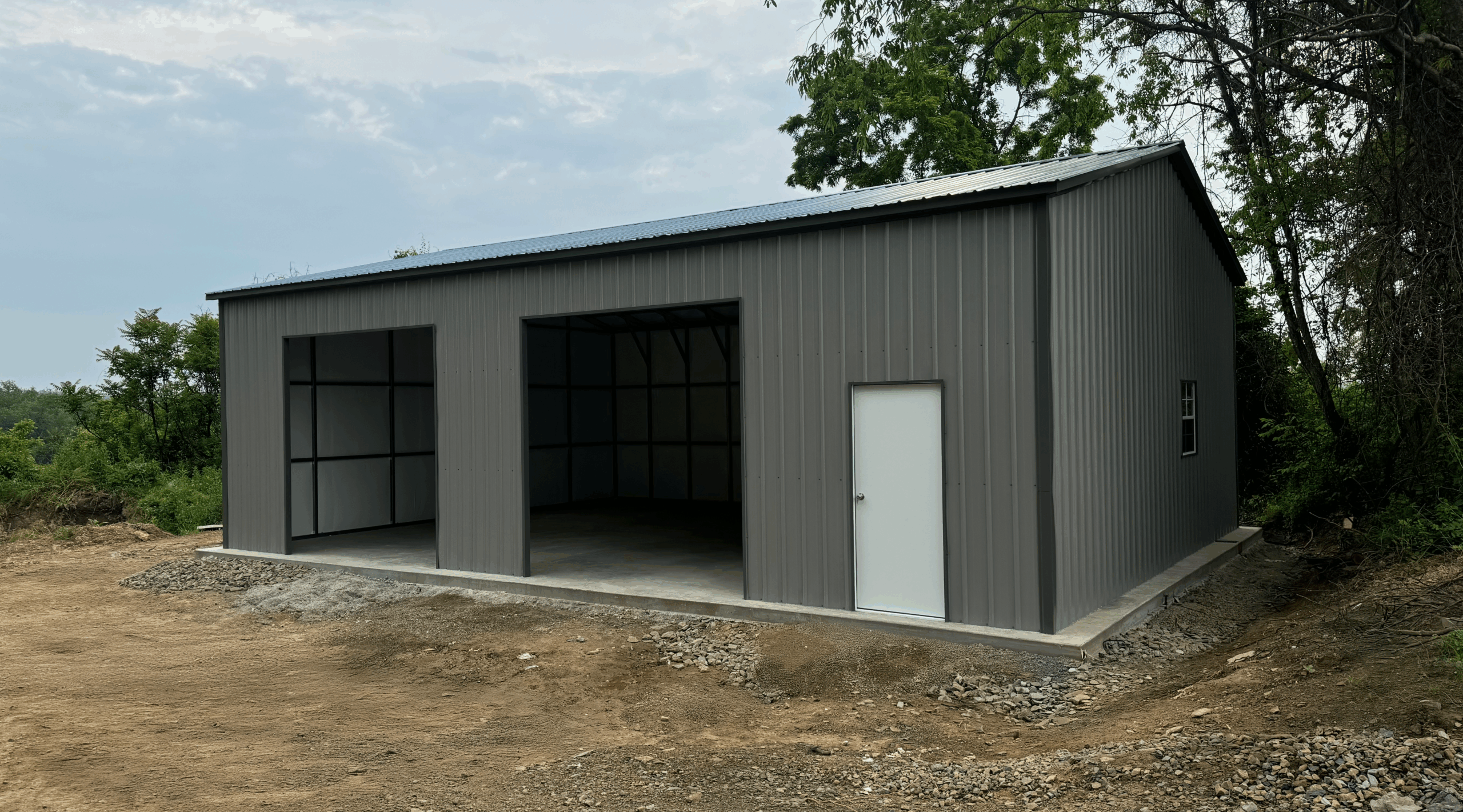 Pewter gray metal garage with two open bays, a white walk-in door, and vertical siding, installed in Albert Lea, Minnesota by American Steel Carports, Inc.