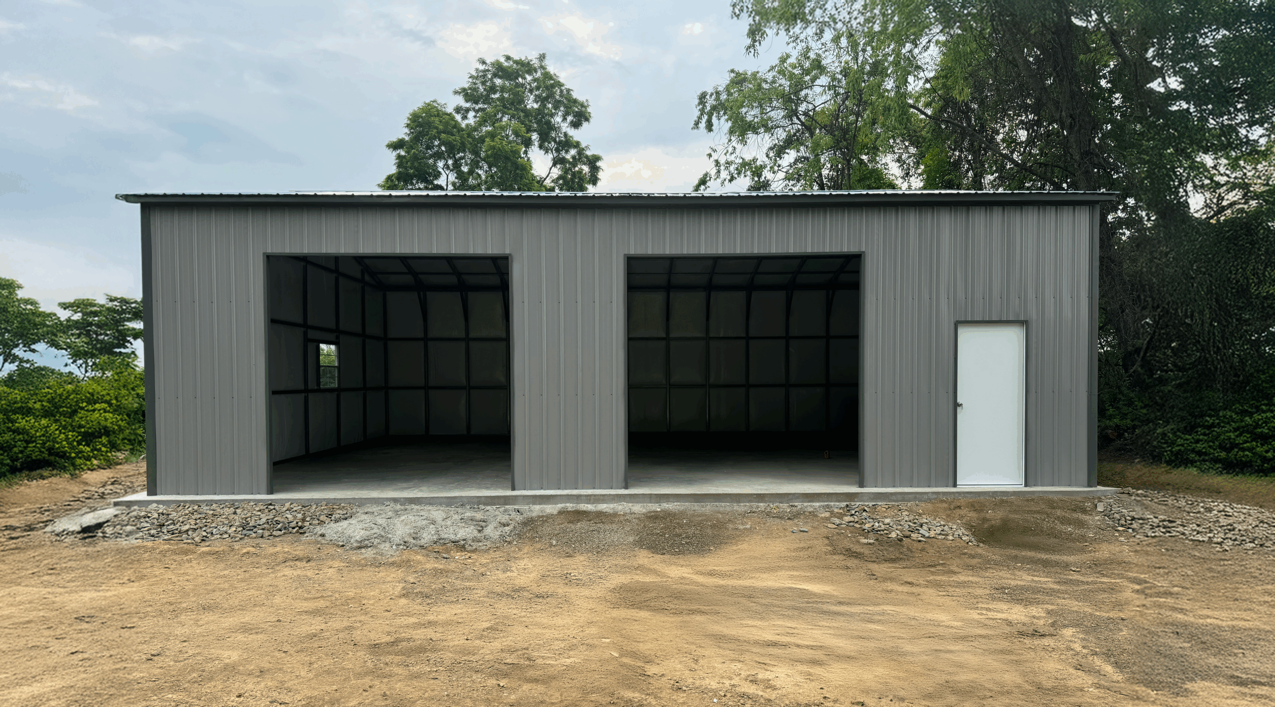 This pewter gray metal garage, equipped with two open bays, a white walk-in door, and vertical siding, was expertly installed in Albert Lea, Minnesota by American Steel Carports, Inc.
