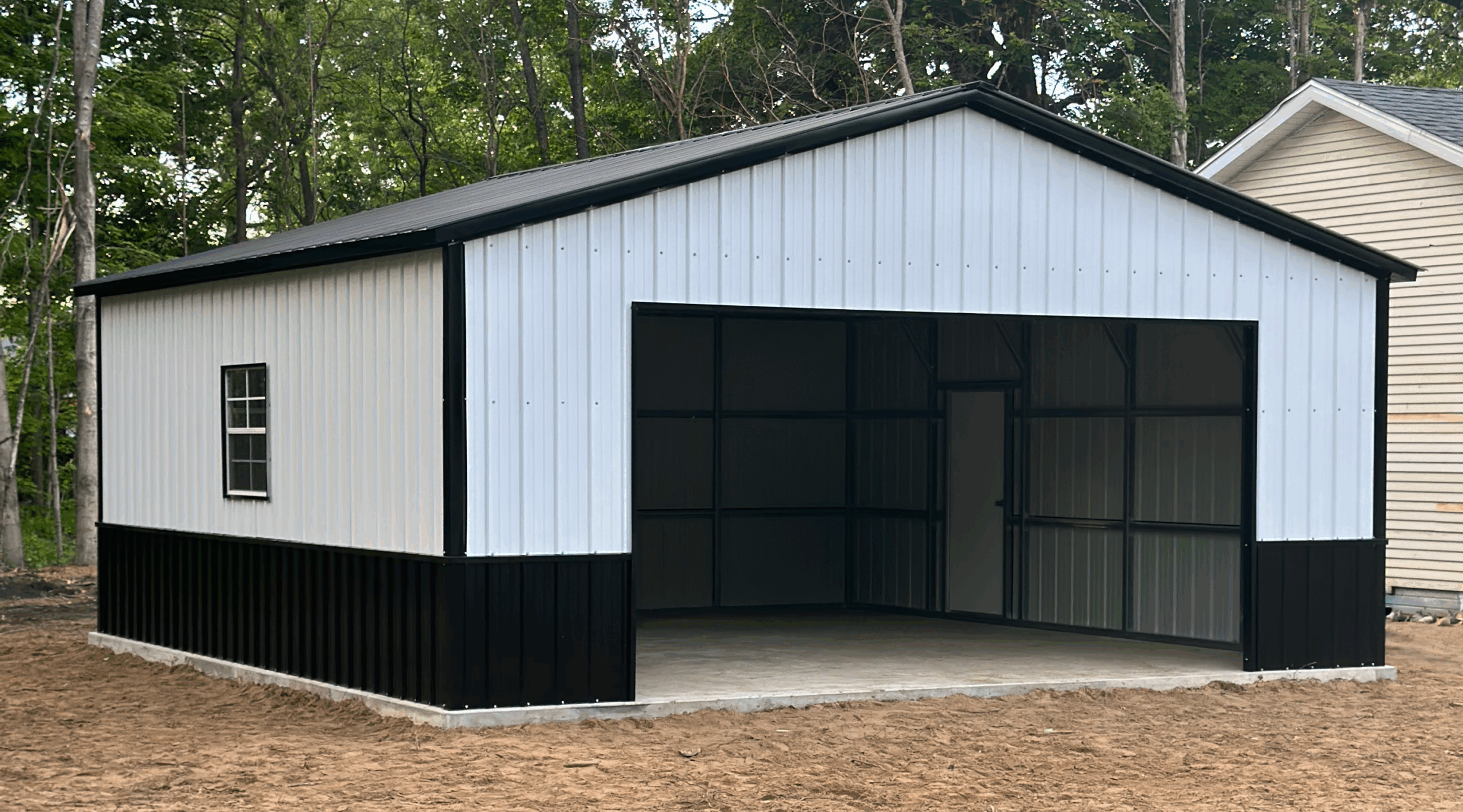 Side view of a black and white steel garage in Alto, TX, showing walk-in door and vertical panel siding.